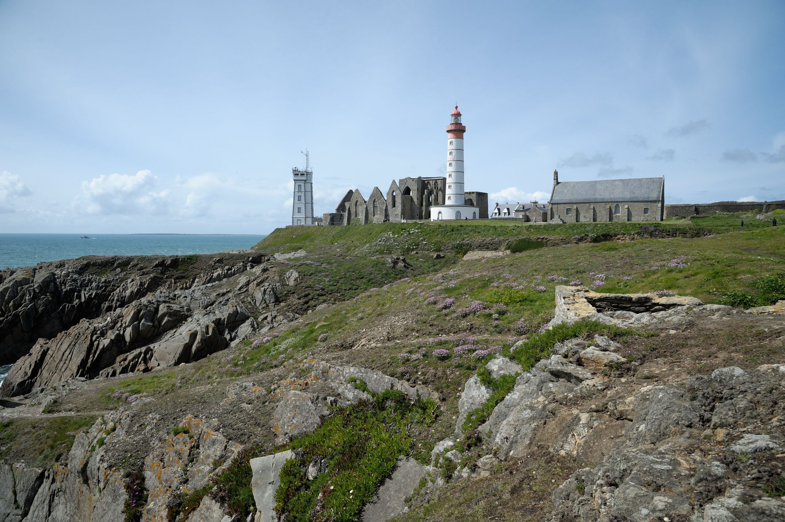 Lighthouse and buildings on the rocky coast of Brittany, France under a clear sky.